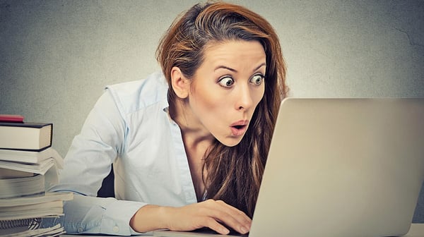 Portrait young shocked business woman sitting in front of laptop computer looking at screen isolated grey wall background. Funny face expression emotion feelings problem perception reaction-1